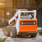 Skid loader stands in front of entrance to new multi-storey house and waits for garbage to be loaded into bucket. Mini bulldozer waiting for cargo in front of porch